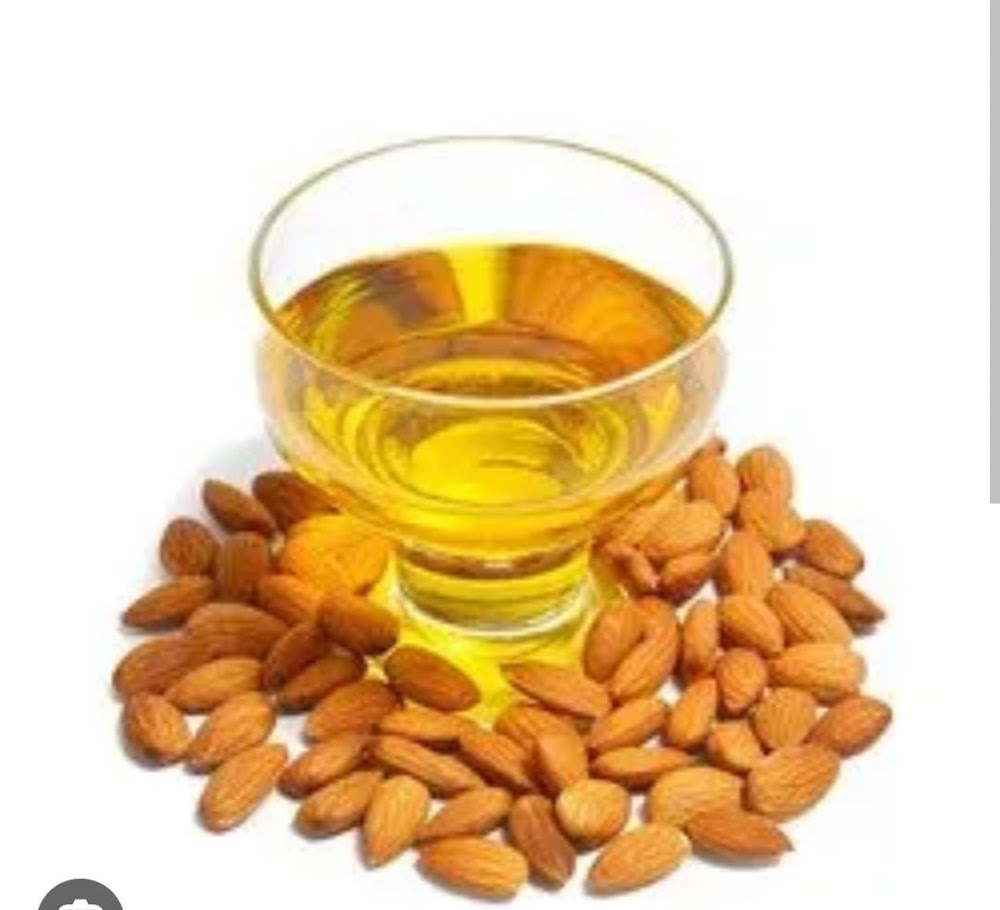 Glass of almond oil surrounded by almonds